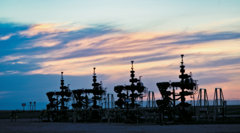 Silhouettes of oil rigs at dusk.