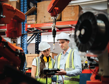 Workers in hard hats looking at an electronic device on a plant floor.